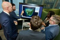 Group stand around informative map on screen with ITOPF team member gesturing towards map. 